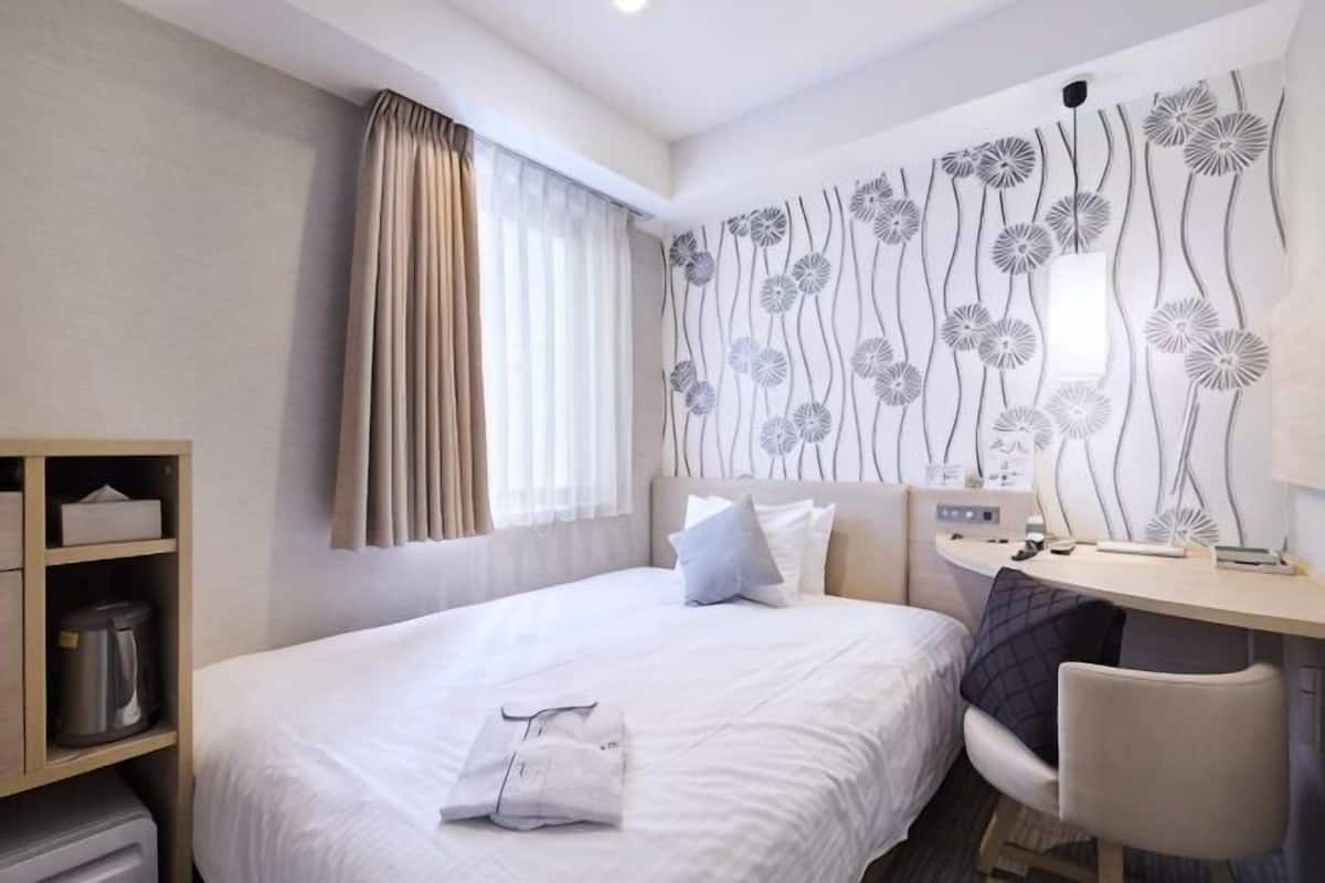 A hotel room with a bed, a desk, a chair, a wardrobe, and a window with curtains.