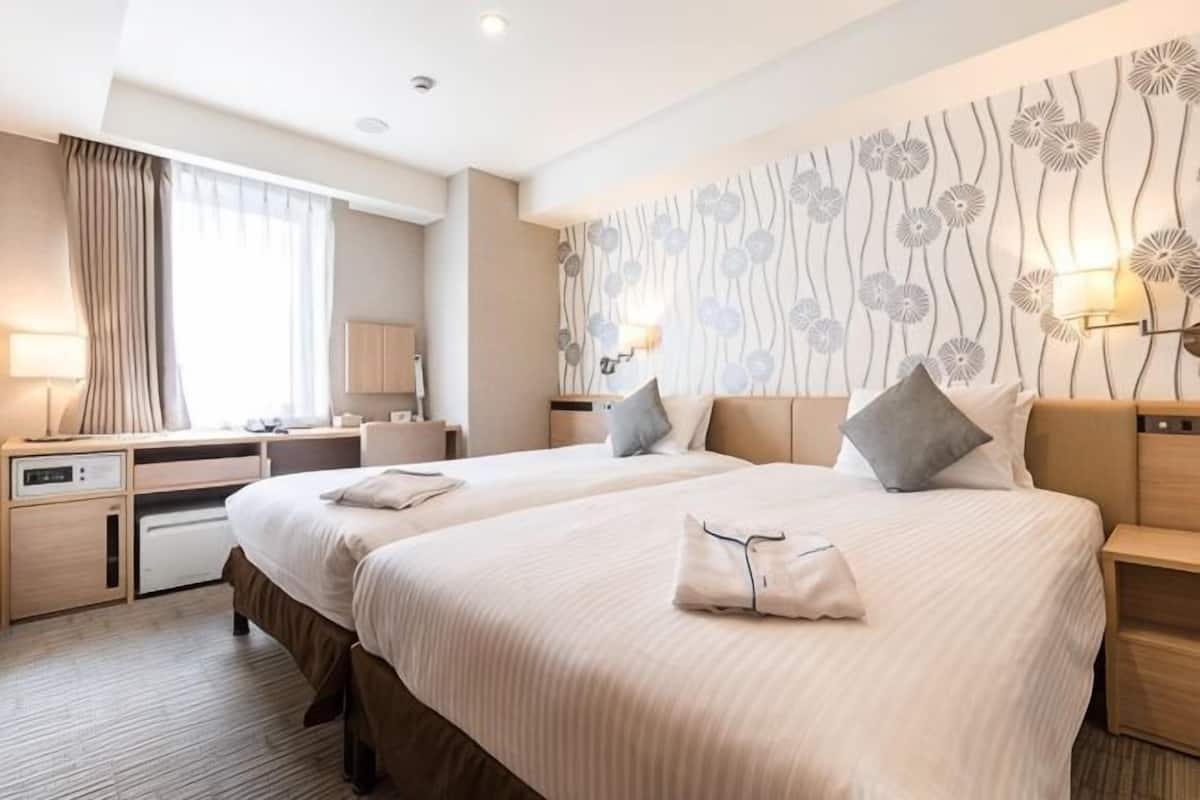 A hotel room with two beds, a desk, a chair, a lamp, and a decorative wall.