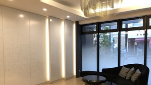 A modern interior with a black sofa, a round table, and large windows offering a view of the street. - Meitetsu Inn Hamamatsucho (Tokyo)