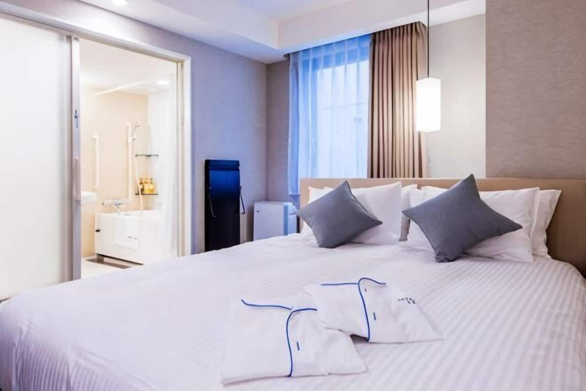 A hotel room with a large bed, a bedside table, a wardrobe, and a bathroom visible through an open door.