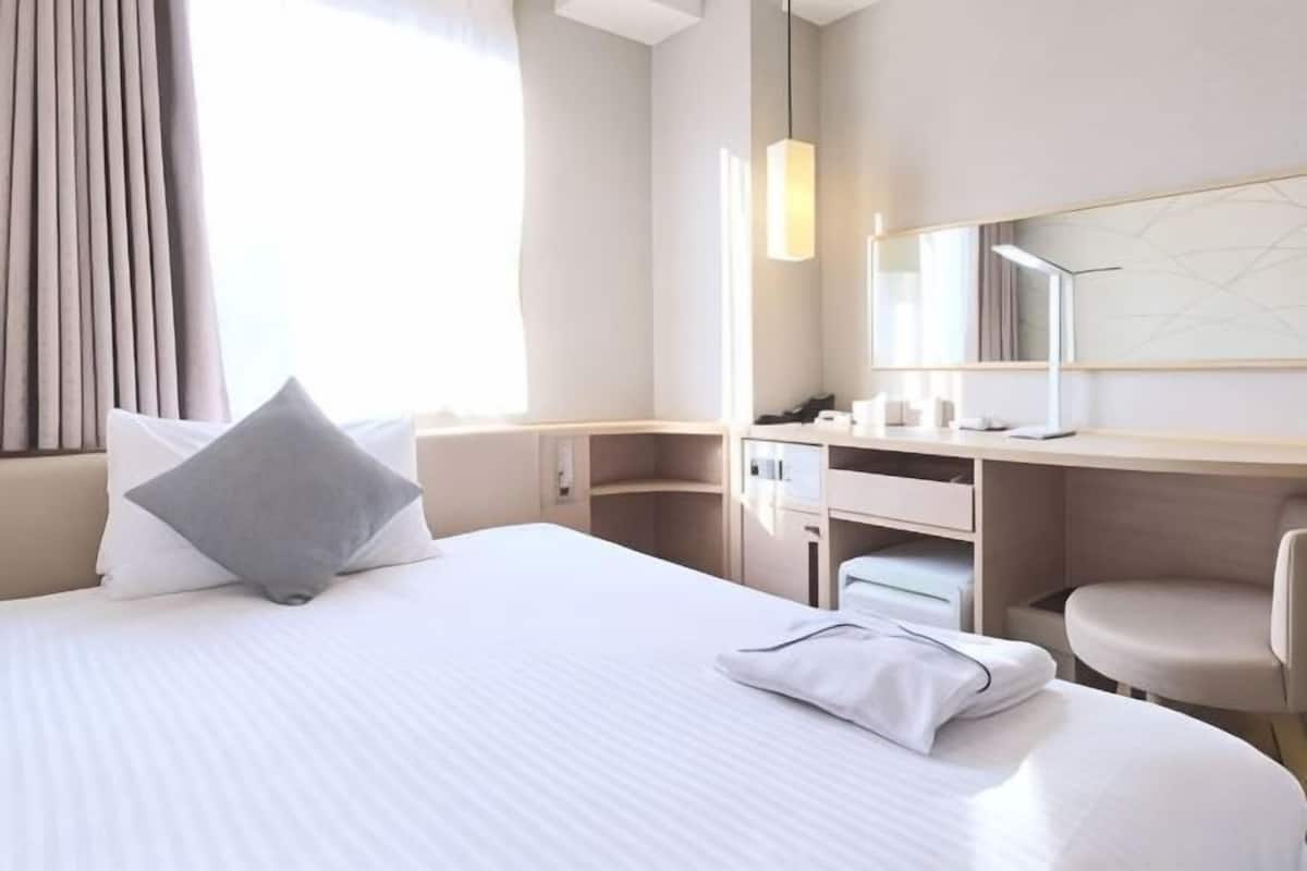 A hotel room with a large bed, a desk, a chair, a mirror, and a window with curtains.