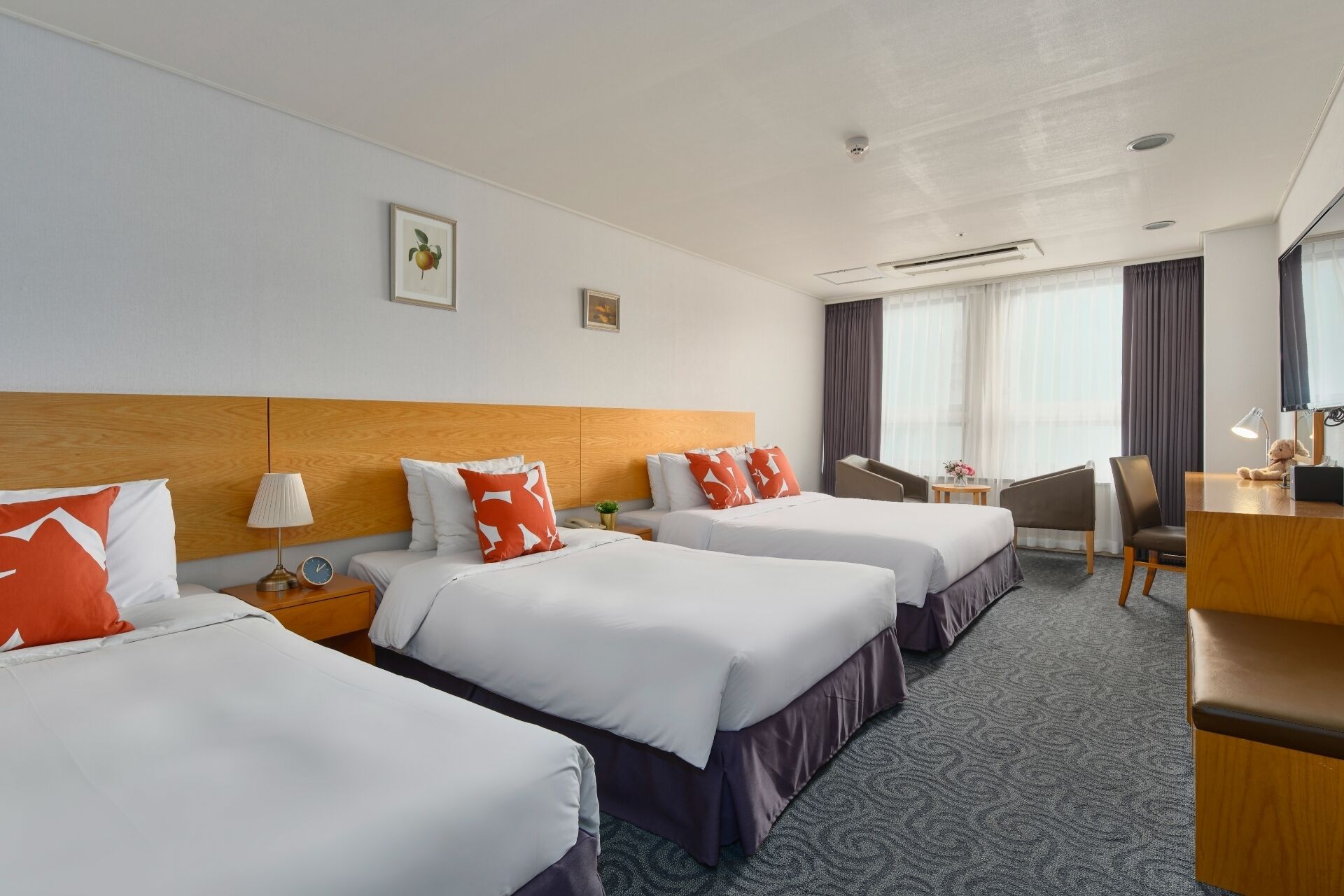 Habitación de hotel con tres camas, un escritorio, una silla y un ventanal con cortinas.