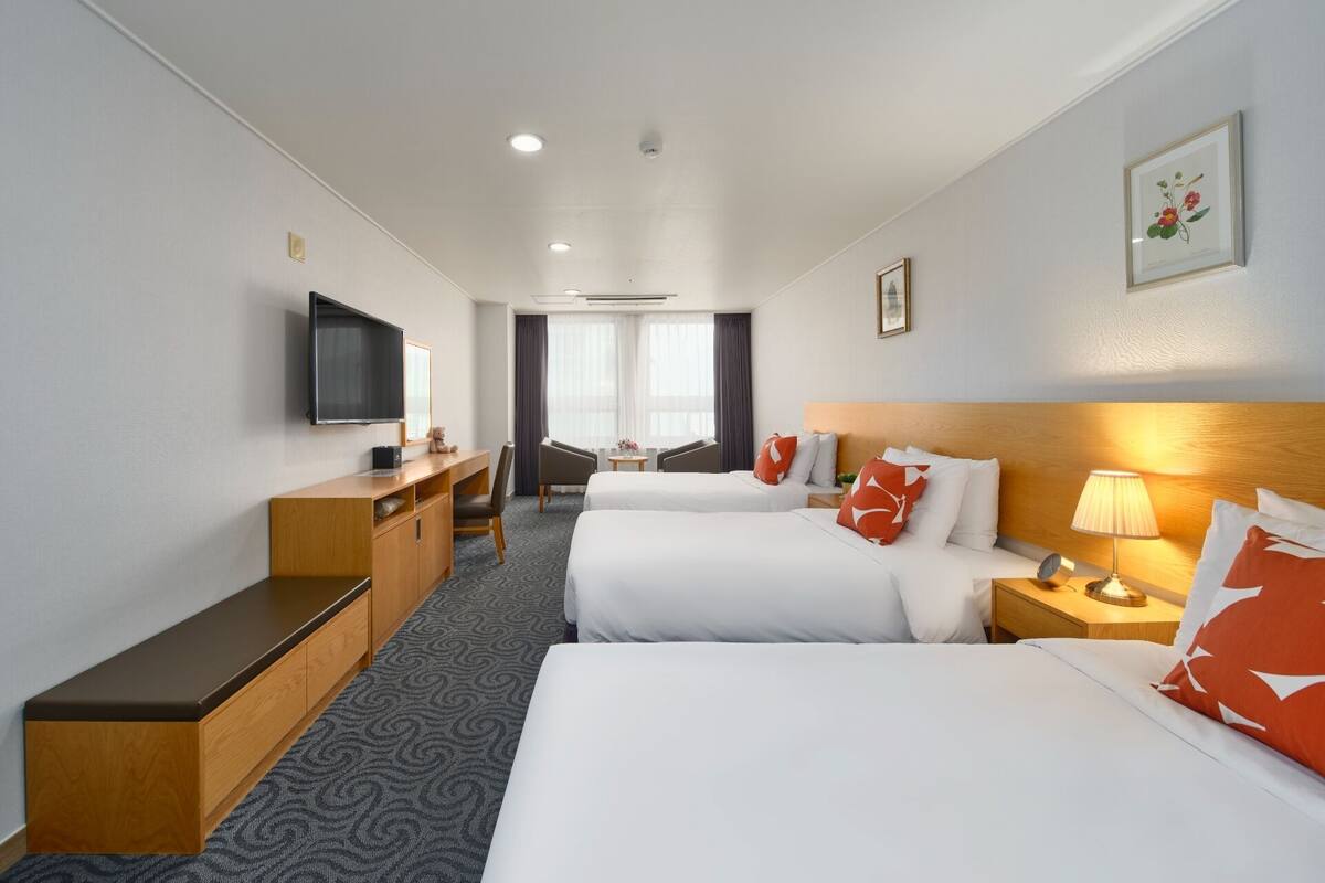 A hotel room with two beds, a desk, a TV, and a window with curtains.