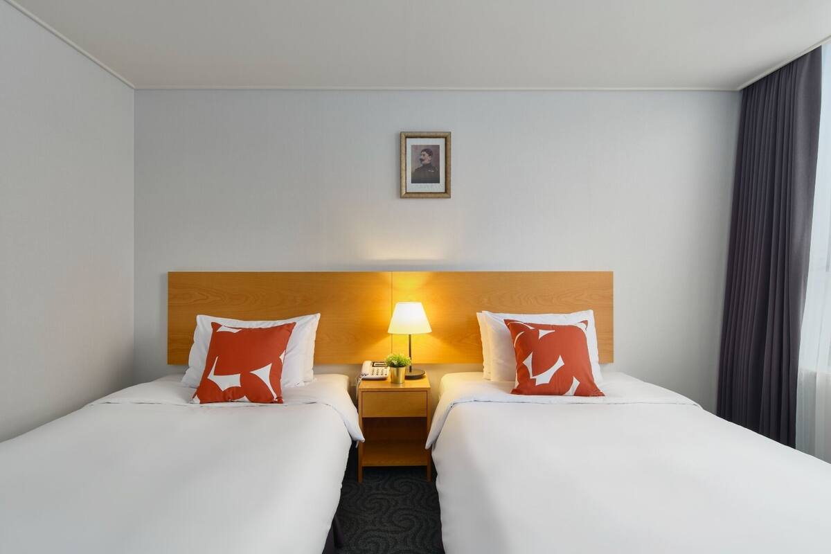 A hotel room with two beds, a wooden headboard, a nightstand with a lamp, and a framed picture on the wall.
