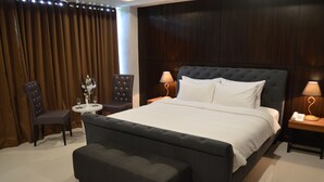 Een slaapkamer met een groot bed, twee nachtkastjes met lampen, een rond bijzettafeltje met een vaas, en een donkere gestoffeerde bank.