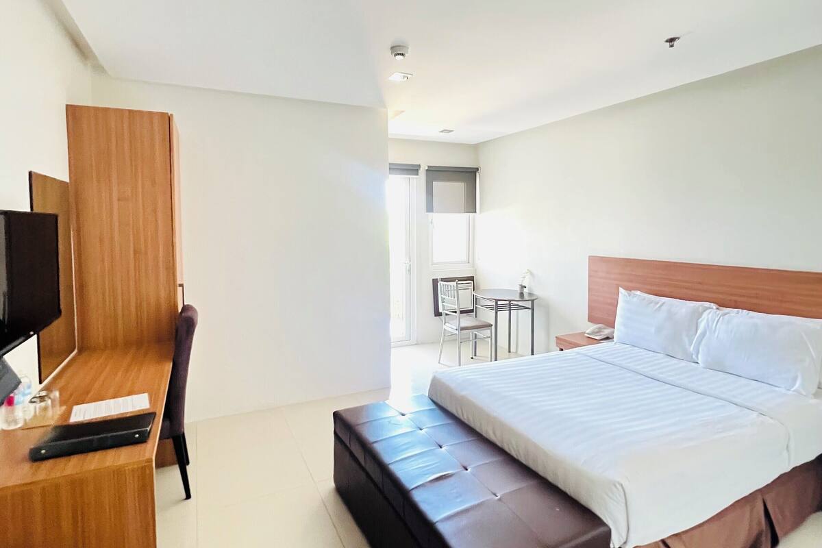 Une chambre d’hôtel avec un lit, un bureau avec un ordinateur, une chaise et une petite table avec une lampe.