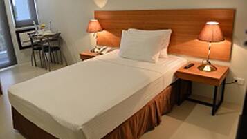 A neatly made bed with a wooden headboard, two bedside lamps, and a small table with a chair beside the bed.