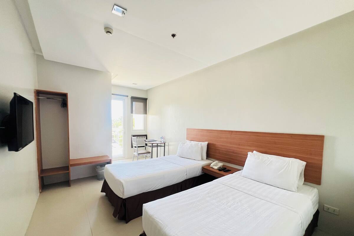Une chambre d’hôtel avec deux lits, un bureau, une chaise et un téléviseur.