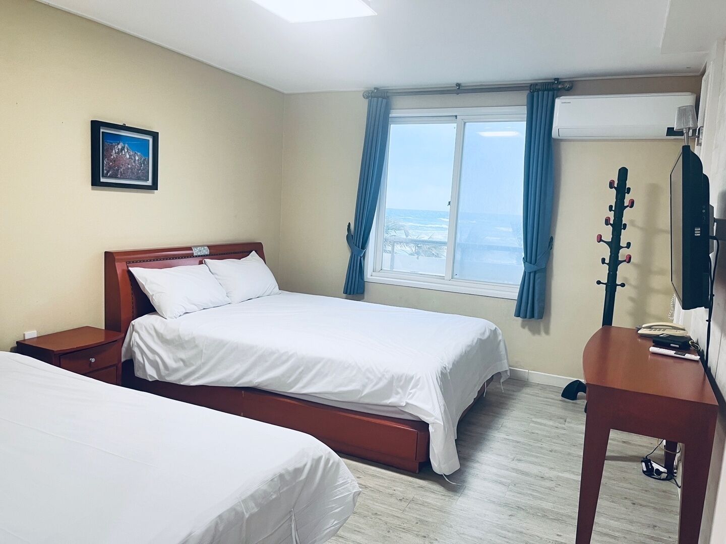 A hotel room with two beds, a desk, a guitar, and a window with a view.
