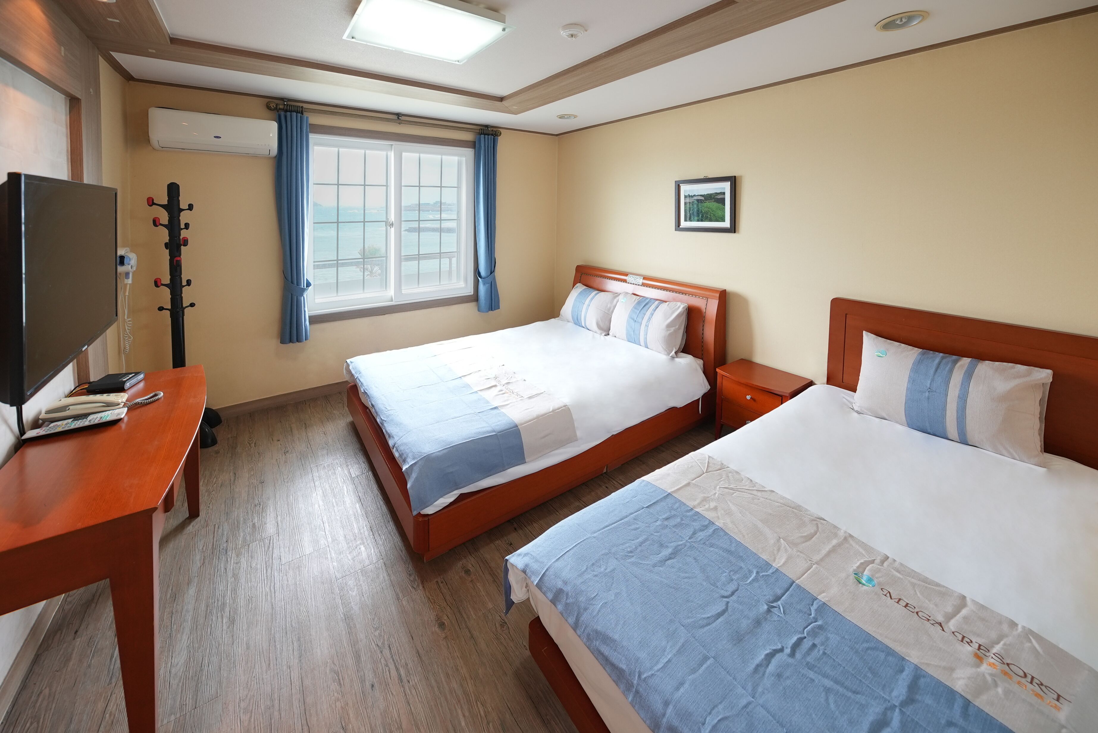 A hotel room with two beds, a desk, a TV, and a window with curtains.