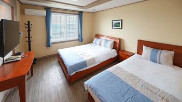 A hotel room with two beds, a desk, a TV, and a window with curtains.