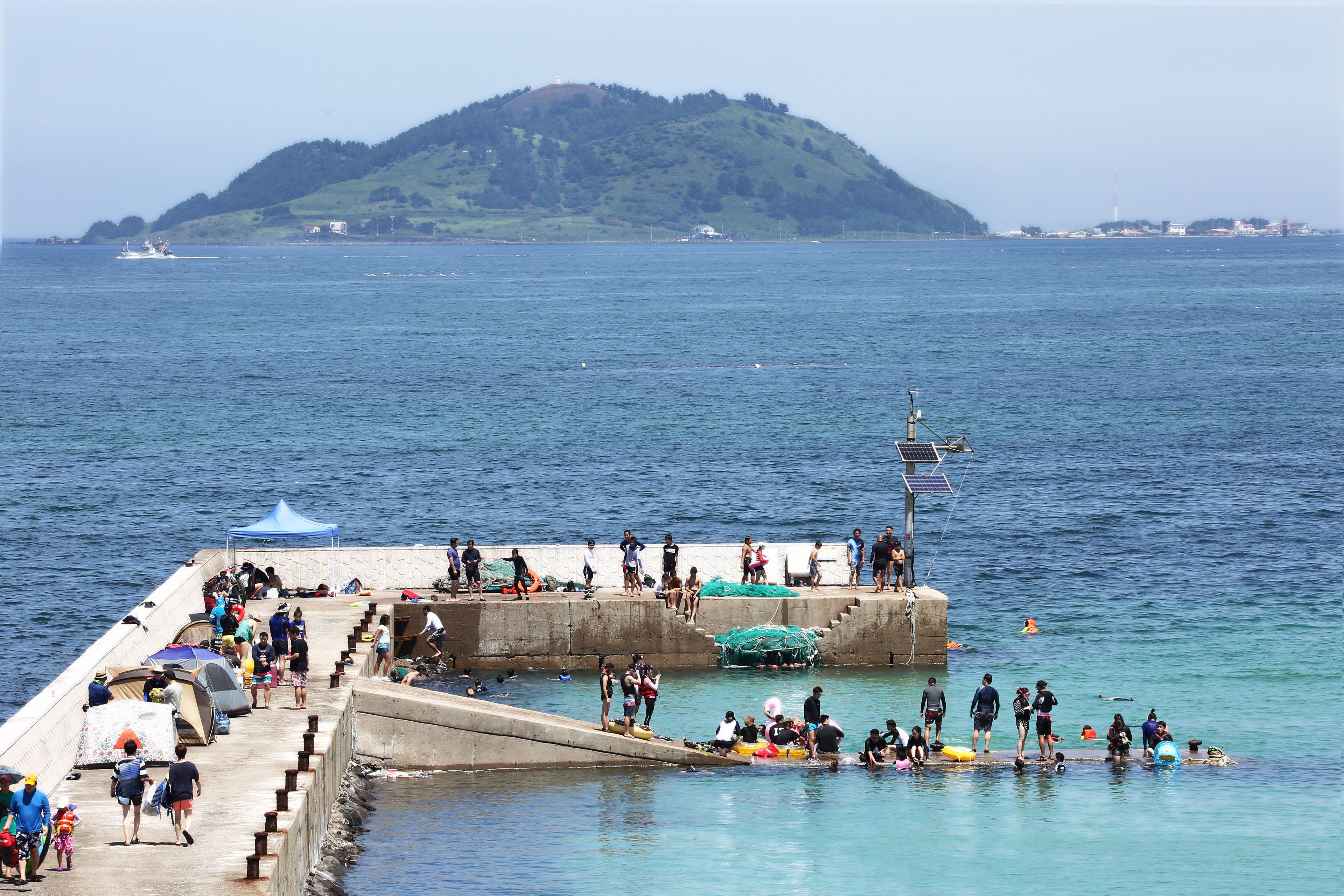 Un muelle con gente caminando, sentada y barcos en el agua.