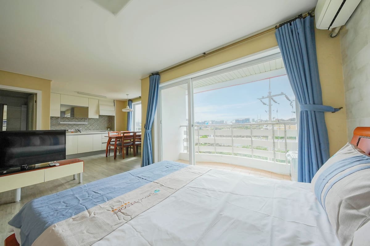 A hotel room with a bed, a TV, a balcony with curtains, and a view of the city.