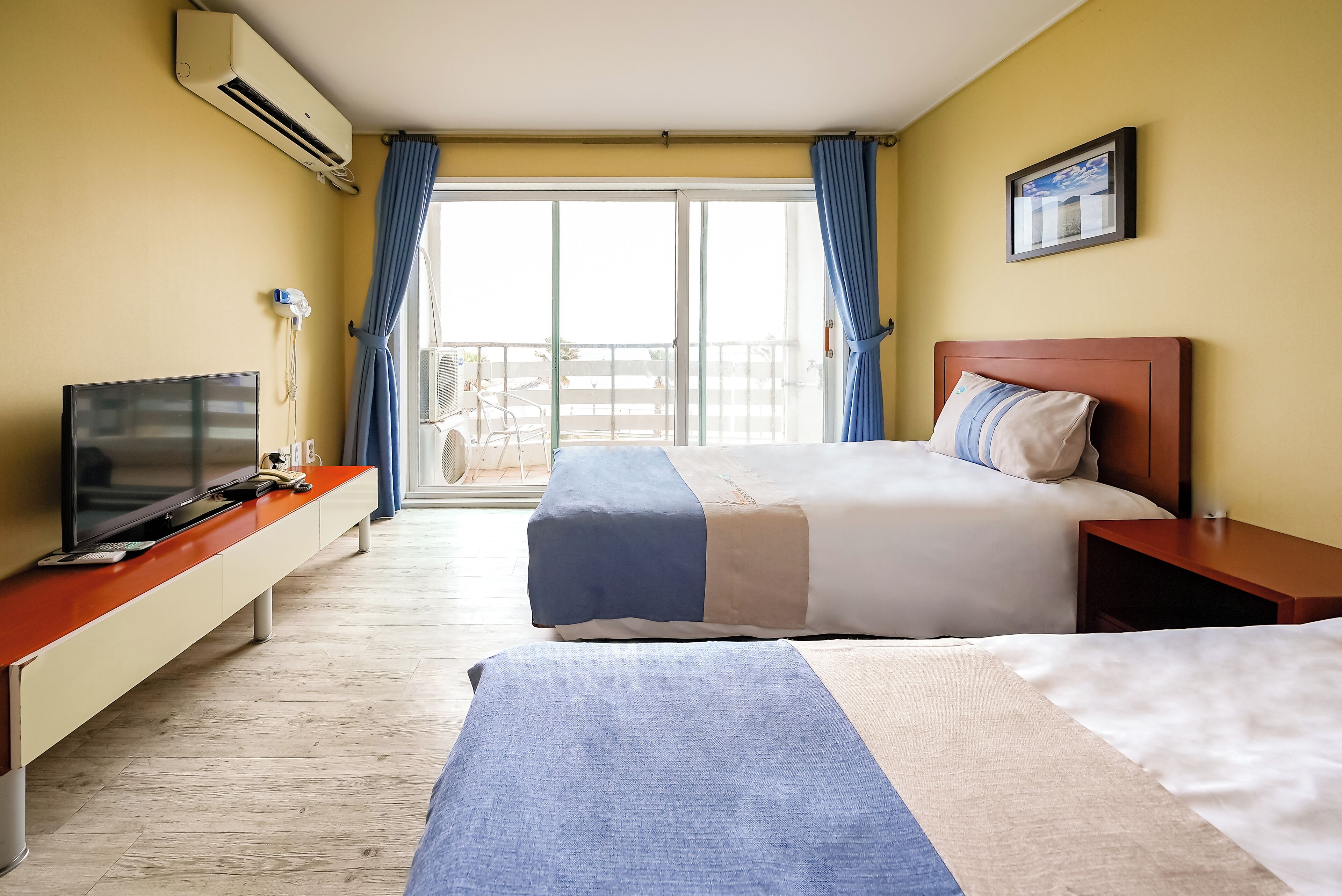 Habitación de hotel con cama, televisor, escritorio y balcón con cortinas.