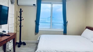 Et hotelværelse med en seng, et skrivebord med en computer, et knagered og et vindue med havudsigt.
