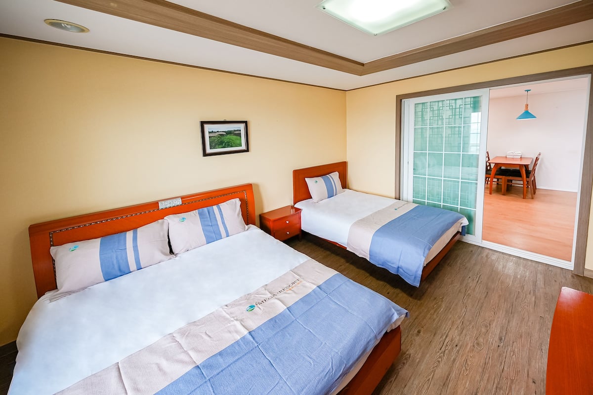 A hotel room with two beds, a small table, and a sliding glass door leading to a balcony.