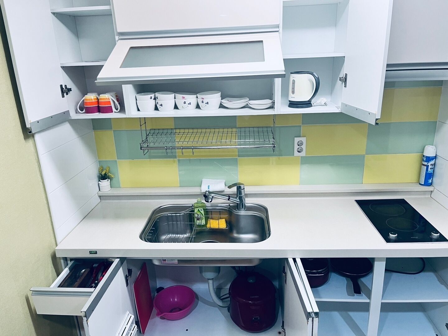 Een kleine keuken met een magnetron, waterkoker en een spoelbak met afwasspons.