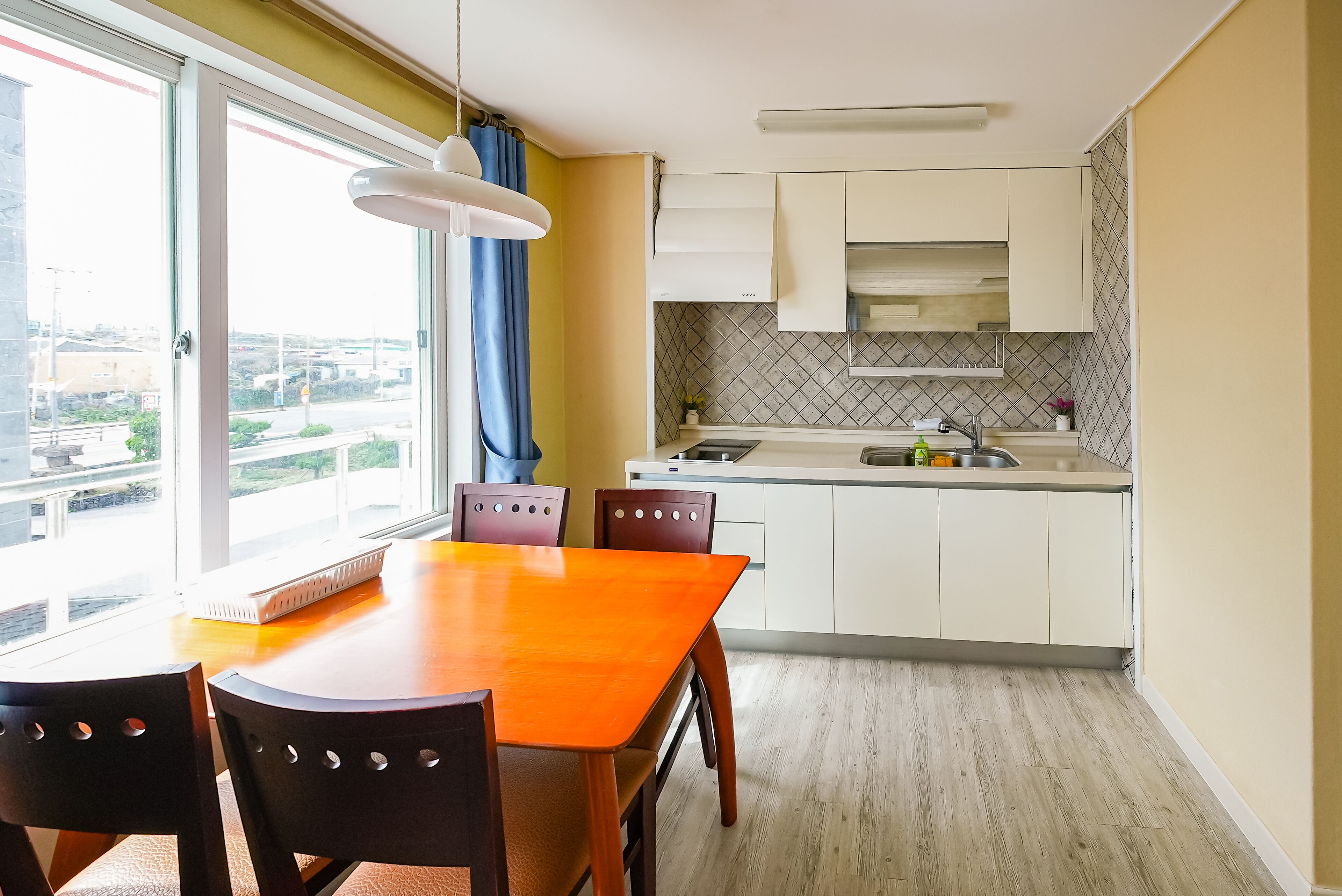 Eine moderne Küche mit weißen Schränken, einem Holztisch und Blick durch das Fenster.
