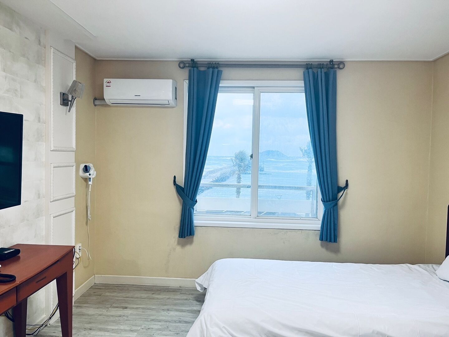 A hotel room with a bed, a desk, an air conditioner, and a window with curtains.