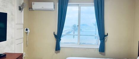A hotel room with a bed, a desk, an air conditioner, and a window with curtains.