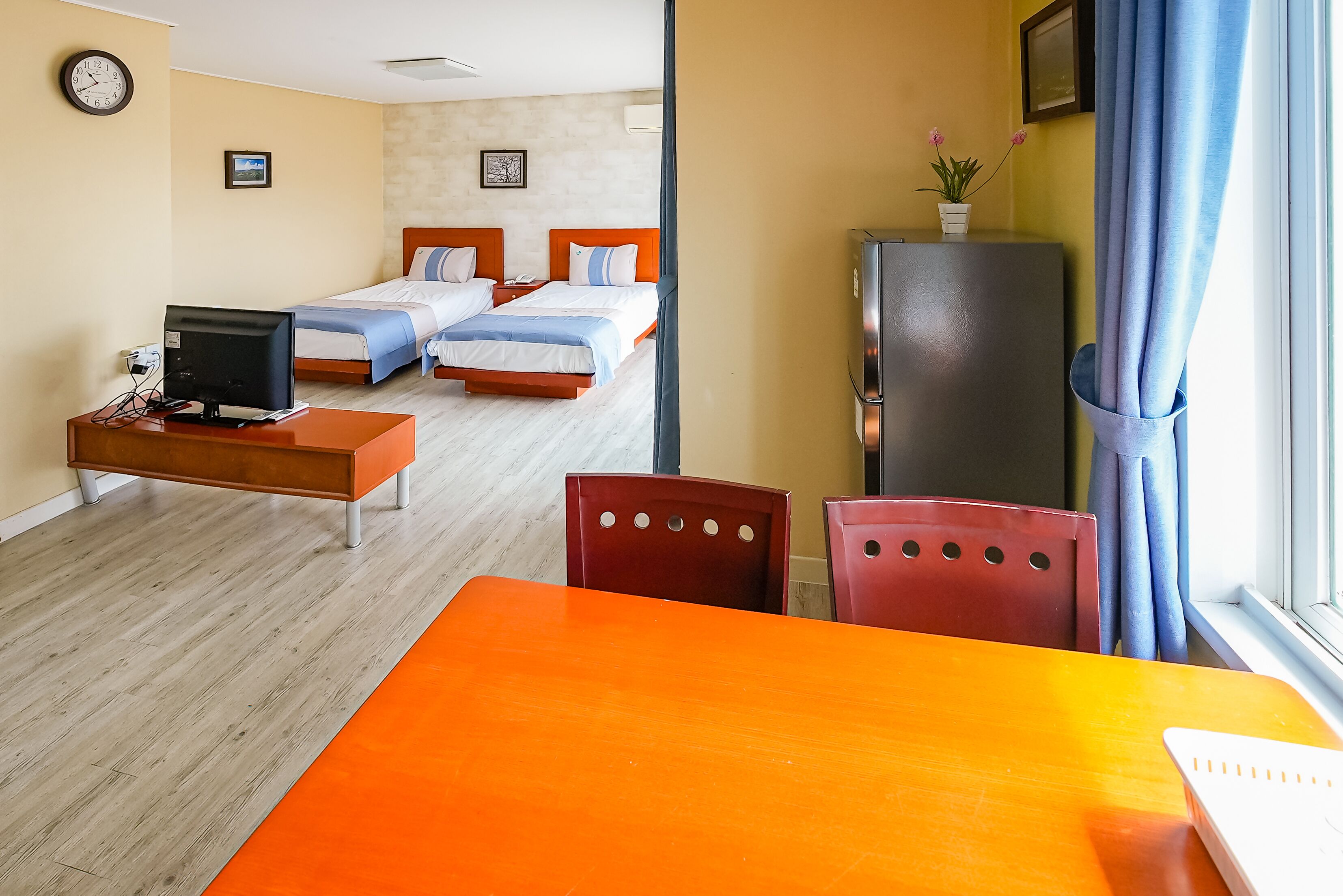 A hotel room with two beds, a desk with a computer, a refrigerator, and a window with curtains.