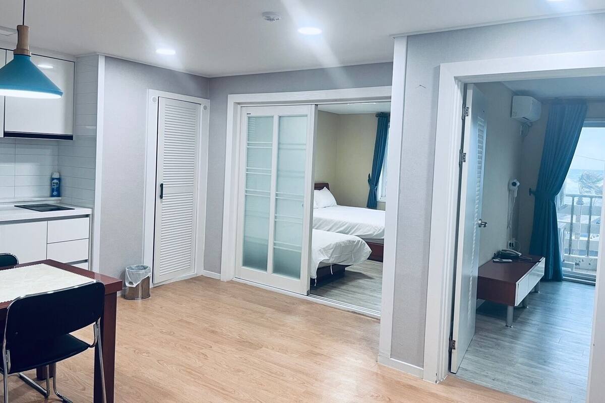 A modern hotel room with a kitchenette, a dining area, and a bedroom with a sliding glass door leading to a balcony.