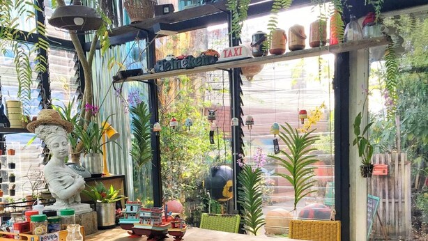 A dining area with a table and chairs, surrounded by various plants and decorative items. - Artist Place Trat (Trat)