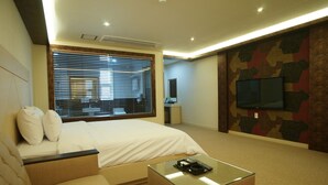 Ein Hotelzimmer mit Bett, einem Glastisch, einem an der Wand montierten Fernseher und einem Fenster mit Jalousien.