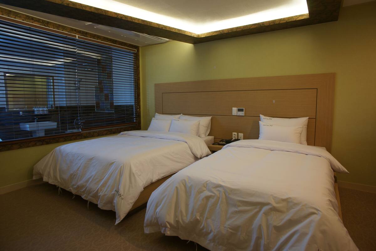 A hotel room with two beds, a window with blinds, and a wooden headboard.