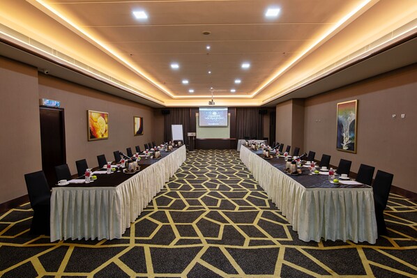 A conference room with a long table, chairs, and a projector screen. - Geno Hotel (Shah Alam)