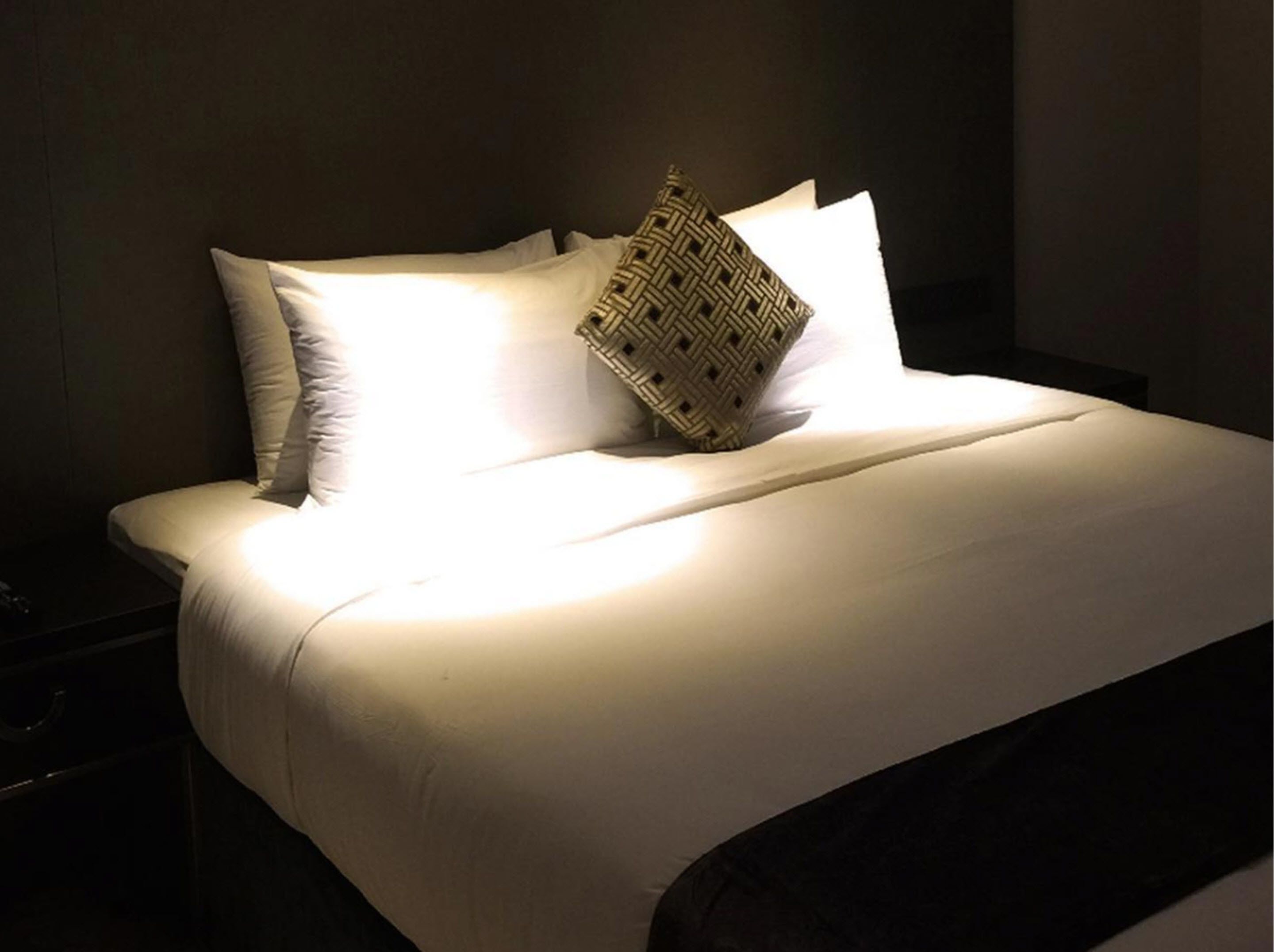 Una cama bien hecha con sábanas blancas y un cojín tejido.