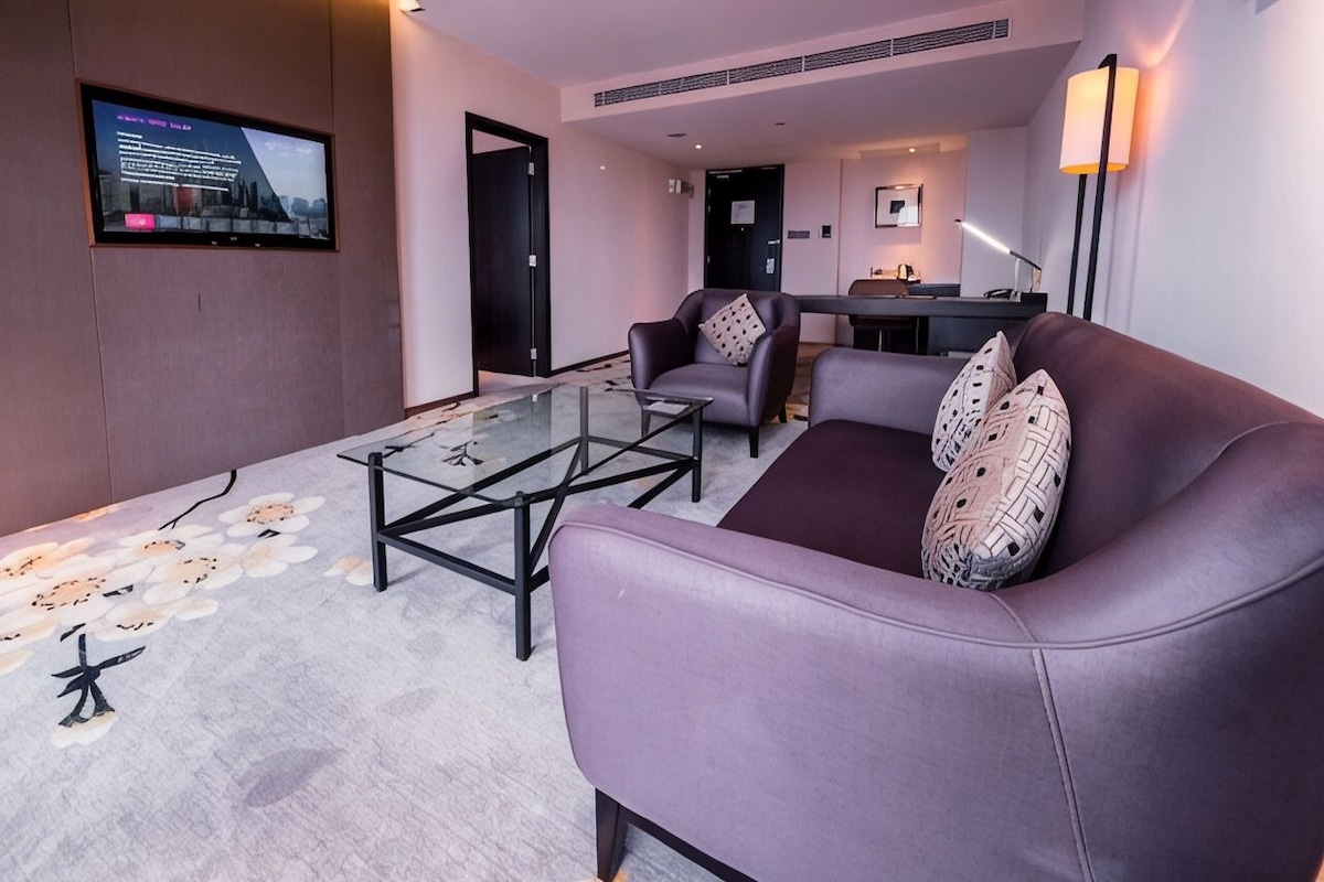 A modern hotel room with a sofa, armchair, and a glass coffee table.