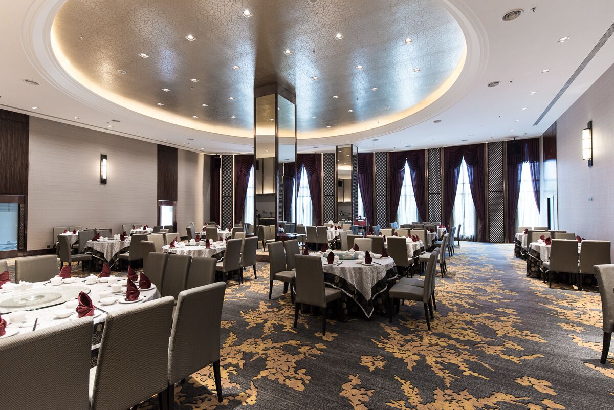 A large, well-lit conference room with round tables and chairs, a patterned carpet, and a modern ceiling design.