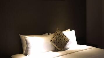 A neatly made bed with white linens and a woven pillow, a bedside table, and a wall-mounted light fixture.