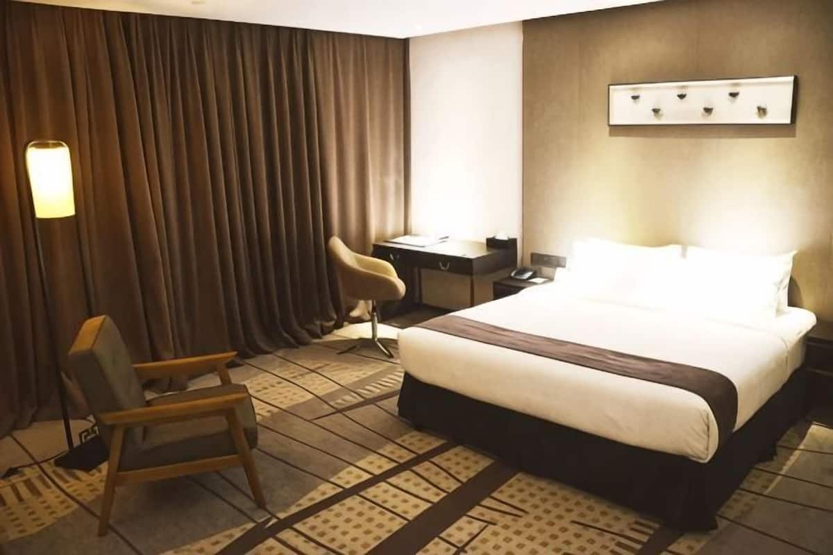 A hotel room with a bed, a desk, a chair, a lamp, and a wall-mounted light fixture.