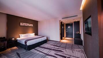A modern hotel room with a large bed, a desk, and a seating area.