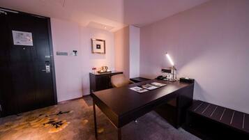 A hotel room with a dark wooden desk, a chair, a small cabinet, and a bed with a headboard.