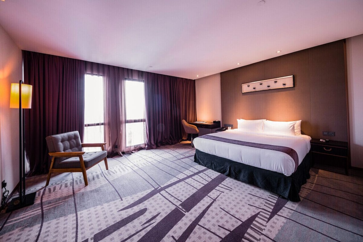 Hotellihuone, jossa on suuri sänky, työpöytä, tuoli ja lattiavalaisin.