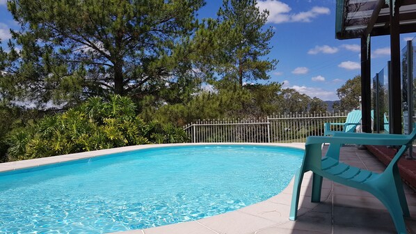 A swimming pool with clear blue water, surrounded by lush greenery and a white fence. - Serendipity On Barrington (Barrington)