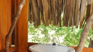 A rustic outdoor bathroom with a wooden structure, a white sink, and a green towel hanging on a branch. - Beddegama Eco (Thissamaharama)