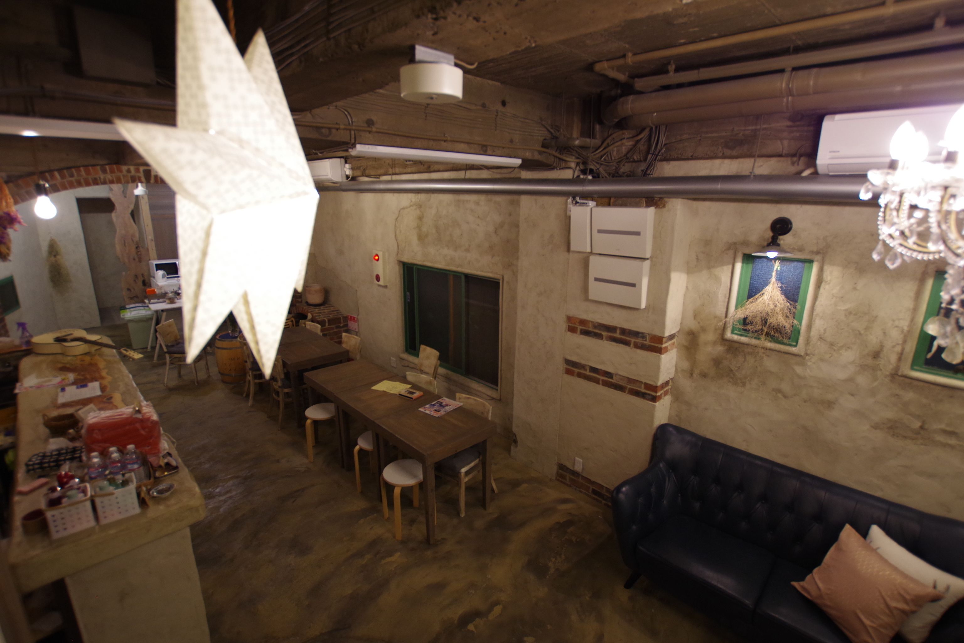 Un interior rústico con una mesa de comedor de madera, sillas, un sofá azul oscuro y una lámpara decorativa grande.