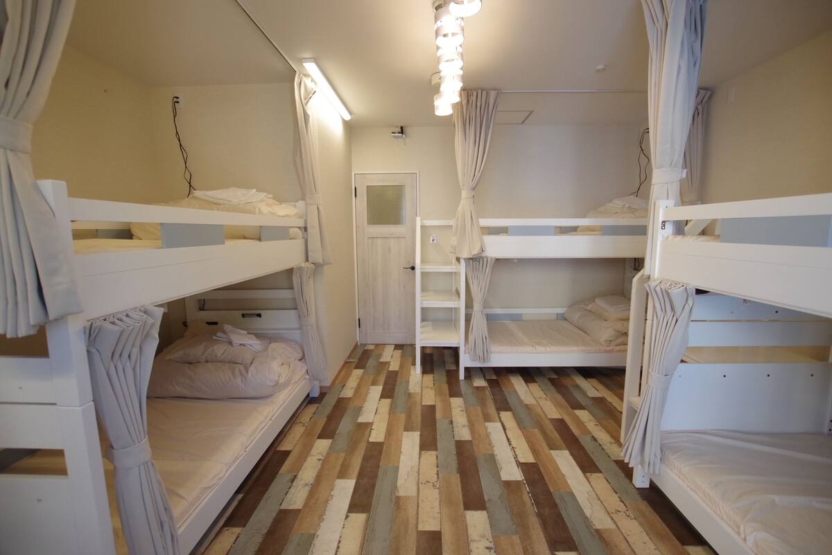 Une pièce avec des lits superposés, un parquet en bois et une porte.