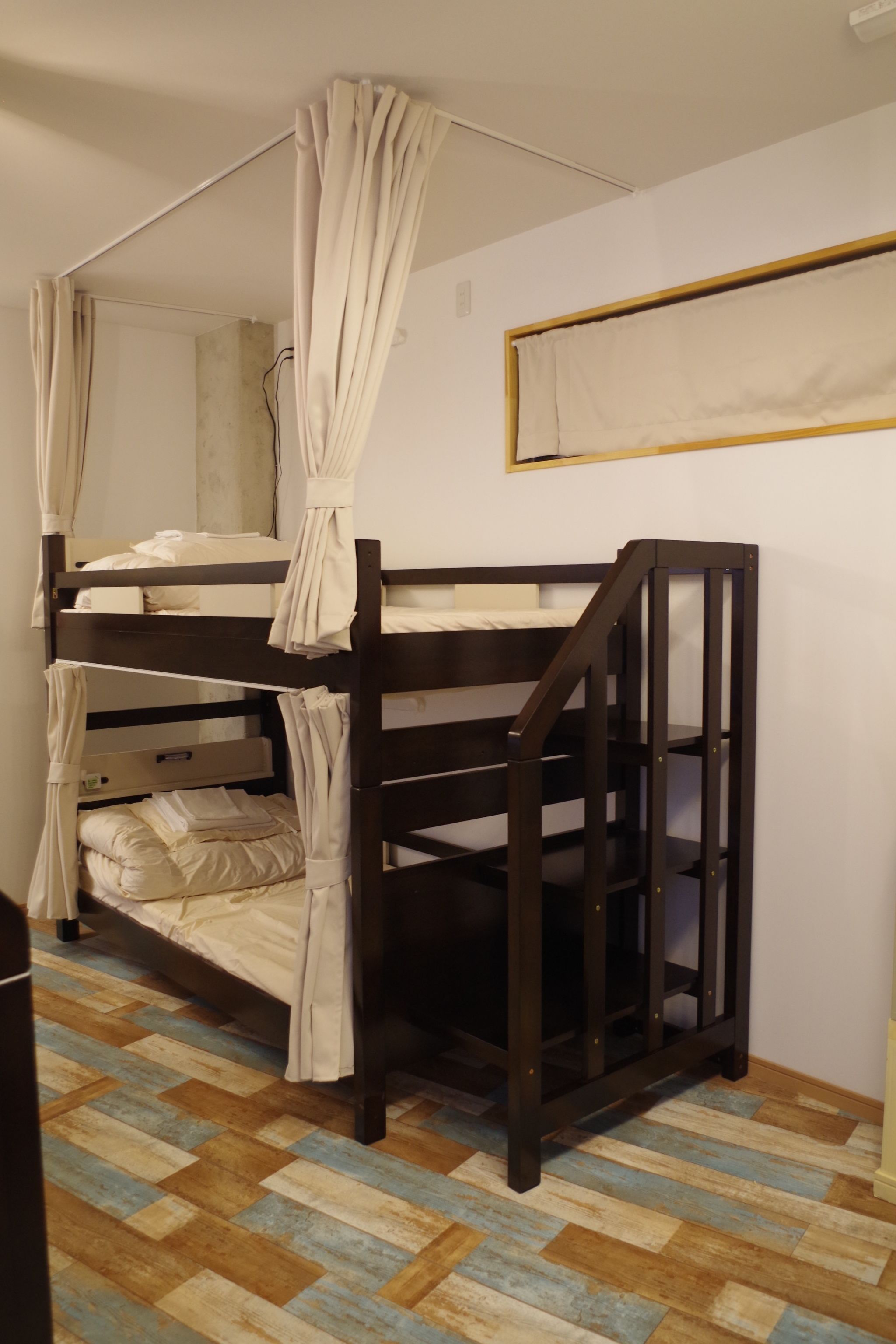 A bunk bed with curtains, a wooden floor, and a wall-mounted mirror.