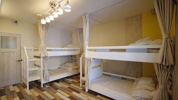 A room with bunk beds, a wooden floor, and a curtain.
