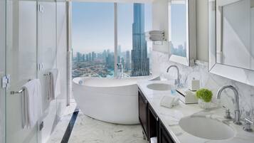 A modern bathroom with a large bathtub, two sinks, and a large mirror. It features a city view with a tall skyscraper.