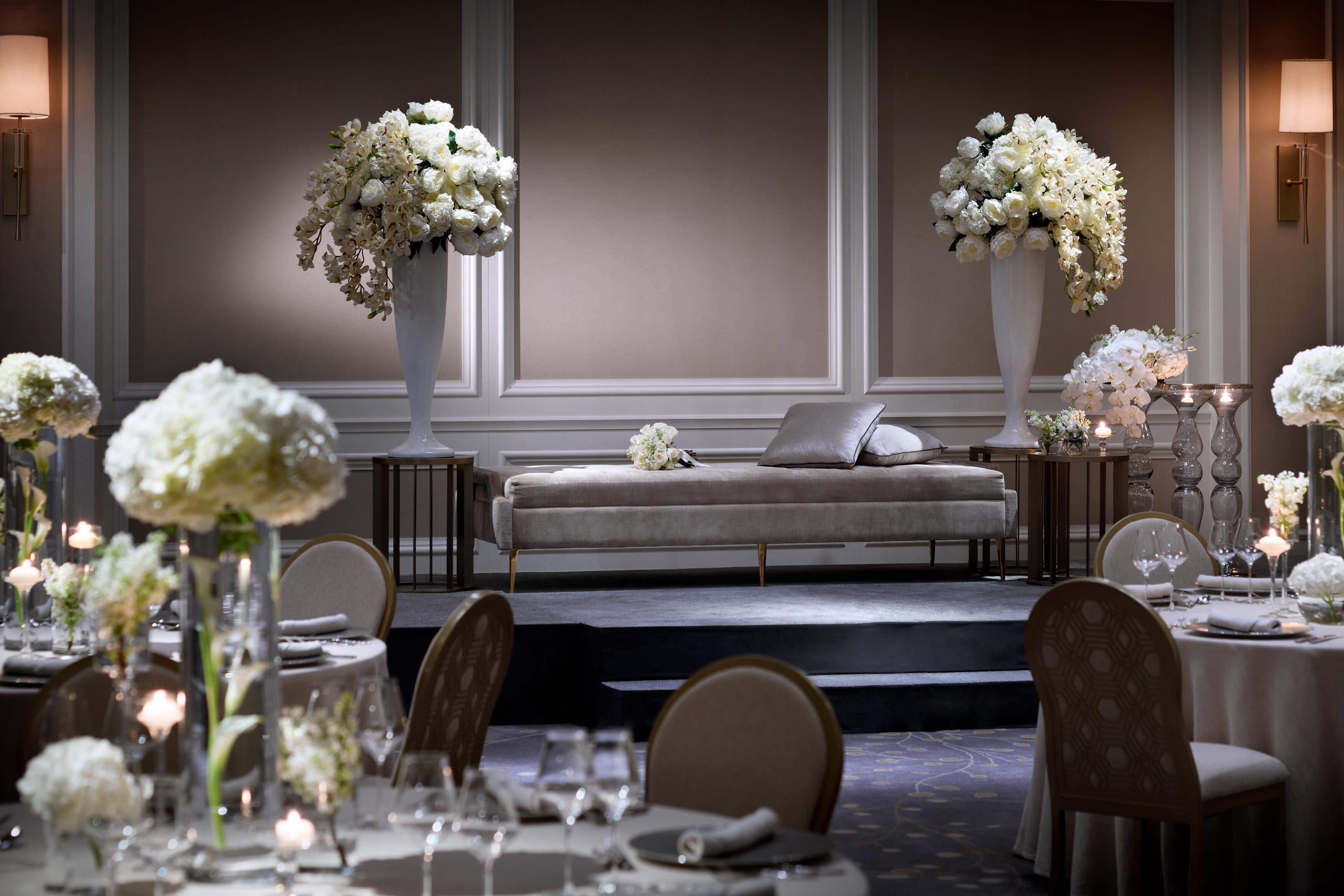 Een statige eetzaal met een podium, elegante stoelen en tafels gedekt voor een maaltijd.