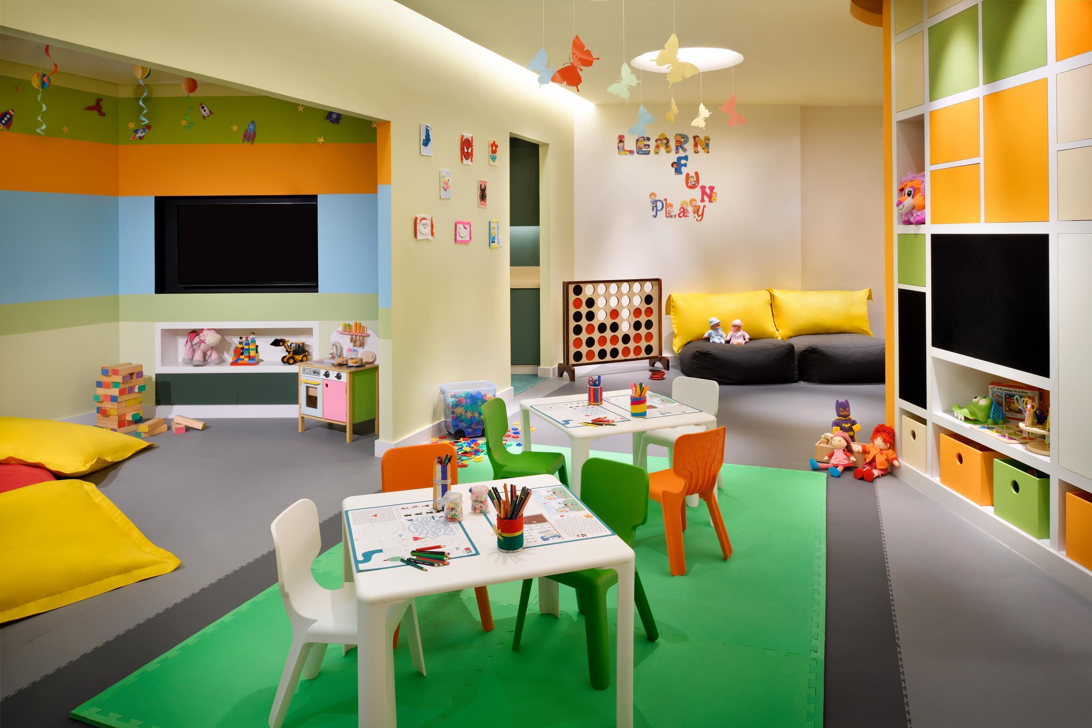 Uma sala de jogos infantil com mobiliário colorido, televisão e decoração educativa.