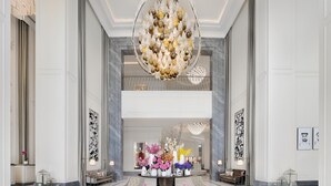 Un hall d’entrée spacieux, agrémenté d’une table ronde centrale décorée de fleurs, flanqué de coins salon et surmonté d’un grand lustre.