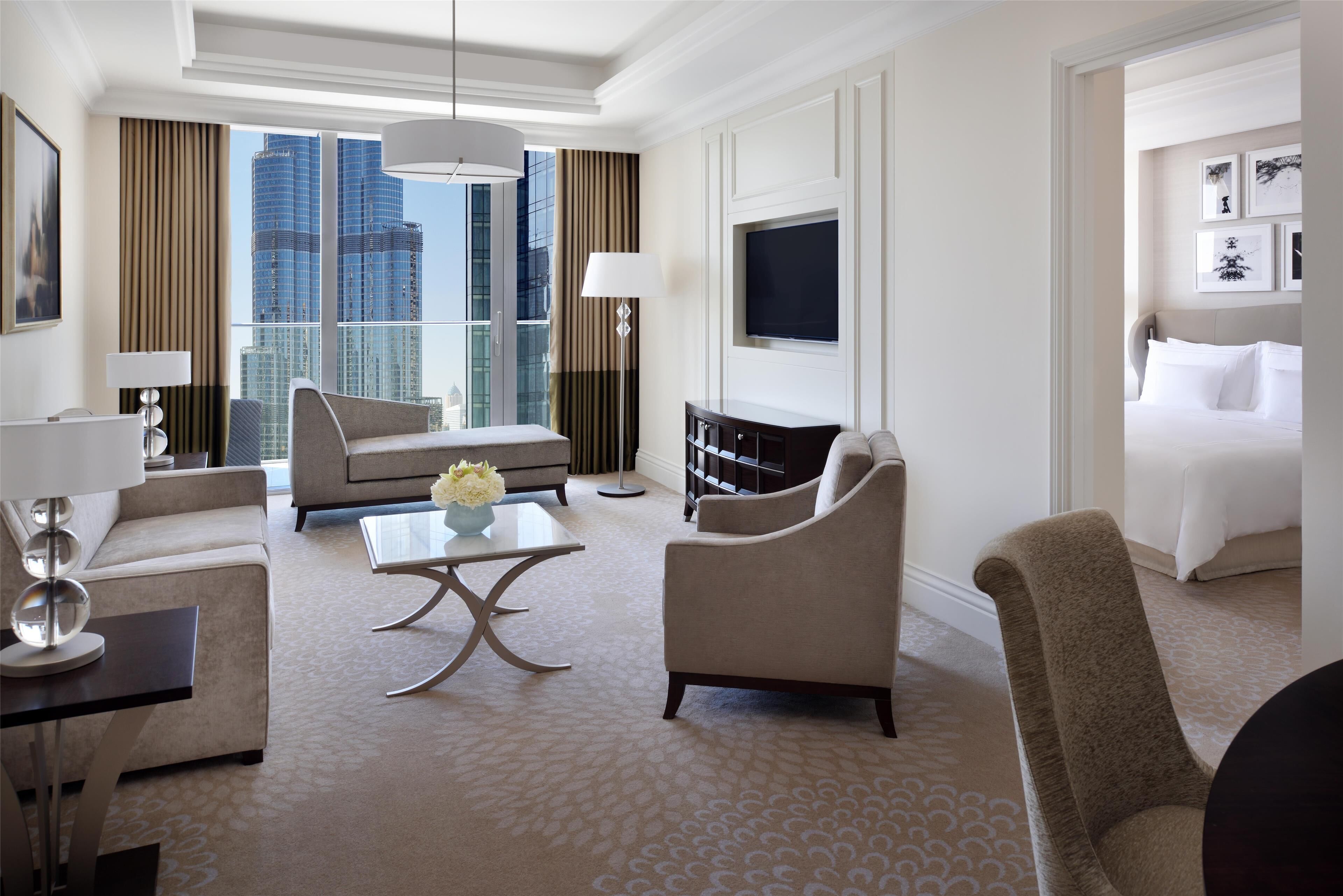 A hotel room with a large window, a sofa, a coffee table, a TV, and a bed.