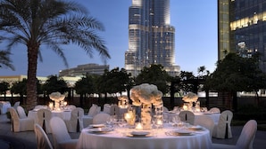 A high-rise building with a distinctive spiral design, surrounded by palm trees and outdoor seating areas with tables and chairs. - Kempinski The Boulevard Dubai (Dubai)